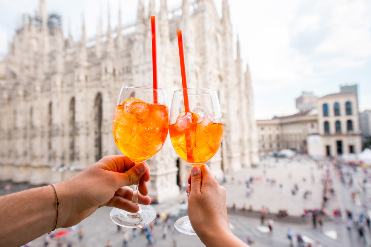 Clinking glasses of spritz aperol drink on the main square with Duomo cathedral on the background in Milan city